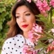a dark-haired white woman on a white t-shirt with black dots bejing some flowers looking to her right
